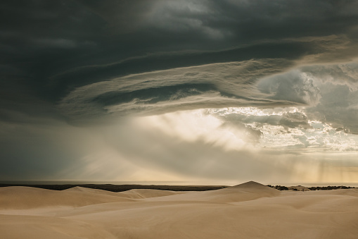 View of dramatic sky and sand dunes in desert. Dark clouds over sand dunes during evening. Moody sky.