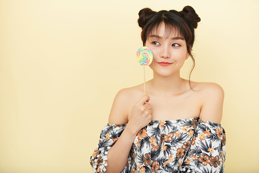 Asian young woman with lollipop isolated on beige background