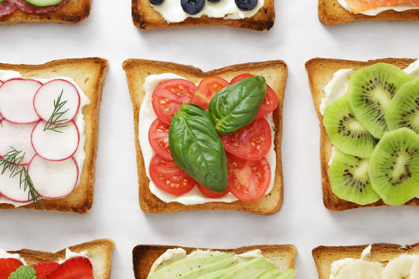 istock Various toasts with tomatoes, basil, cheese, kiwi, radish and other toppings on white parchment. 986496436