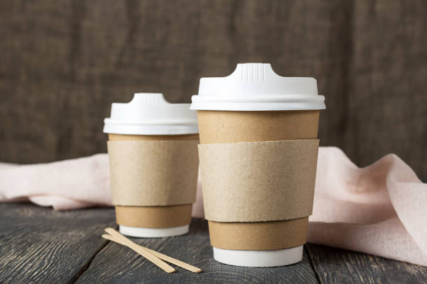 istock Two disposable cups with coffee and wooden stirrers next to light cloth on table 986509500