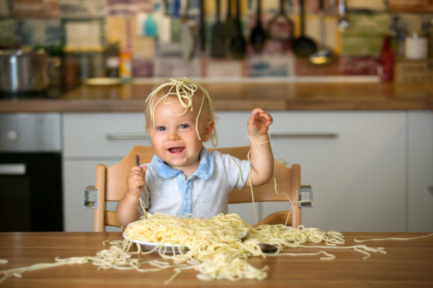 petit bébé garçon, bébé enfant, manger des spaghettis pour déjeuner et faire une bouillie - child eating pasta spaghetti photos et images de collection