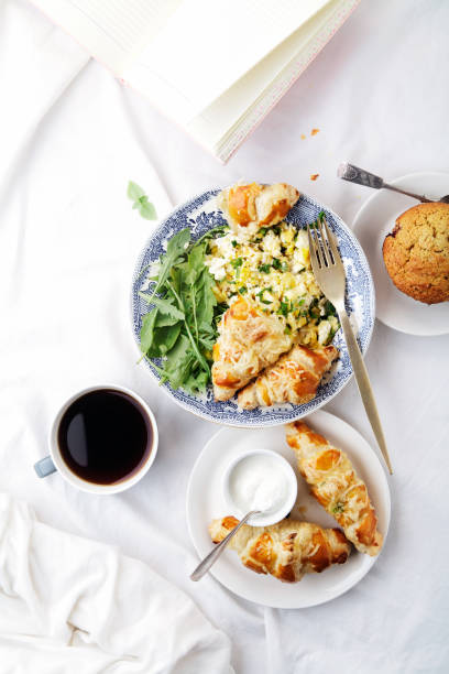 istock Breakfast in bed. Scrambled eggs with cheese croissants, raspberry muffin and black coffee. Morning treat concept. Composition with copy space. 986540622