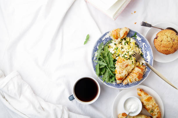 istock Breakfast in bed. Scrambled eggs with cheese croissants, raspberry muffin and black coffee. Morning treat concept. Composition with copy space. 986540636
