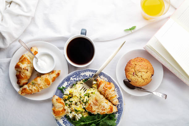 istock Breakfast in bed. Scrambled eggs with cheese croissants, raspberry muffin and black coffee. Morning treat concept. Composition with copy space. 986540644