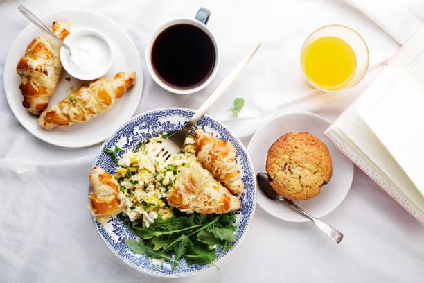 istock Breakfast in bed. Scrambled eggs with cheese croissants, raspberry muffin and black coffee. Morning treat concept. Composition with copy space. 986540684