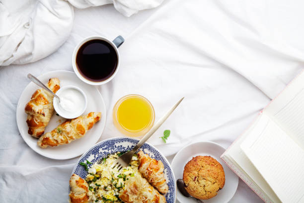 istock Breakfast in bed. Scrambled eggs with cheese croissants, raspberry muffin and black coffee. Morning treat concept. Composition with copy space. 986540696