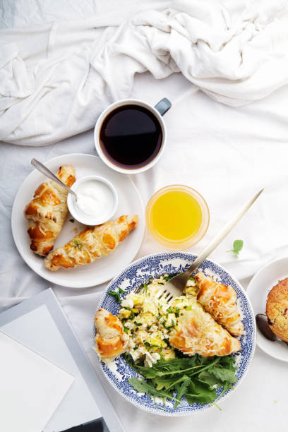 istock Breakfast in bed. Scrambled eggs with cheese croissants, raspberry muffin and black coffee. Morning treat concept. Vertical composition with copy space. 986540698