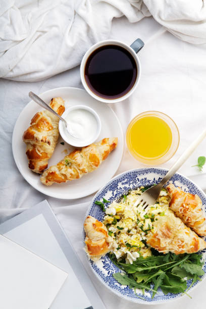 istock Breakfast in bed. Scrambled eggs with cheese croissants, raspberry muffin and black coffee. Morning treat concept. Vertical composition with copy space. 986540700