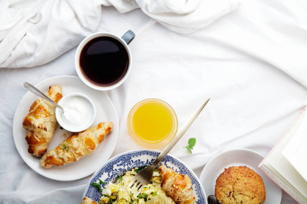 Breakfast in bed. Scrambled eggs with cheese croissants, raspberry muffin and black coffee. Morning treat concept. Composition with copy space.