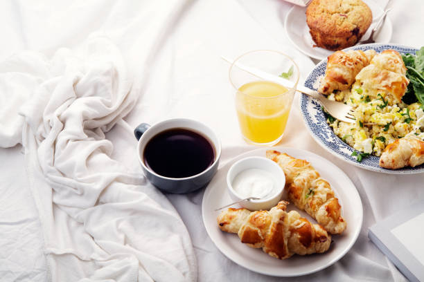 istock Breakfast in bed. Scrambled eggs with cheese croissants, raspberry muffin and black coffee. Morning treat concept. Side view with copy space. 986540724