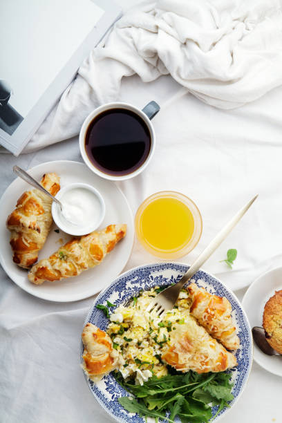 istock Breakfast in bed. Scrambled eggs with cheese croissants, raspberry muffin and black coffee. Morning treat concept. Vertical composition with copy space. 986540726