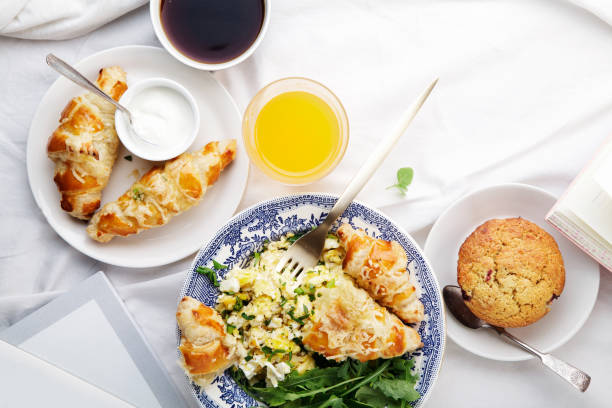 istock Breakfast in bed. Scrambled eggs with cheese croissants, raspberry muffin and black coffee. Morning treat concept. Horizontal composition with copy space. 986540730