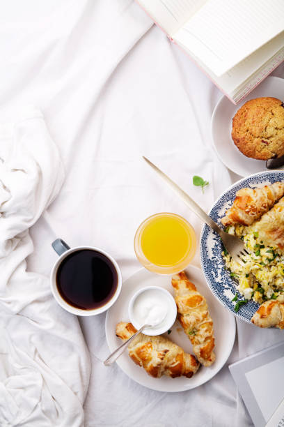 istock Breakfast in bed. Scrambled eggs with cheese croissants, raspberry muffin and black coffee. Morning treat concept. Composition with copy space. 986540736