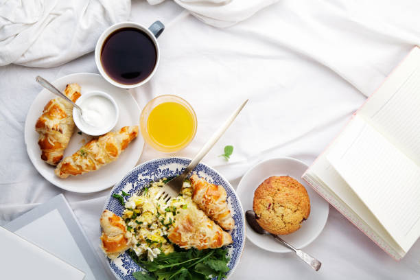 istock Breakfast in bed. Scrambled eggs with cheese croissants, raspberry muffin and black coffee. Morning treat concept. Horizontal composition with copy space. 986540738