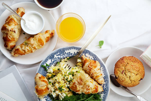 istock Breakfast in bed. Scrambled eggs with cheese croissants, raspberry muffin and black coffee. Lazy morning concept. Flat lay with copy space. 986540760