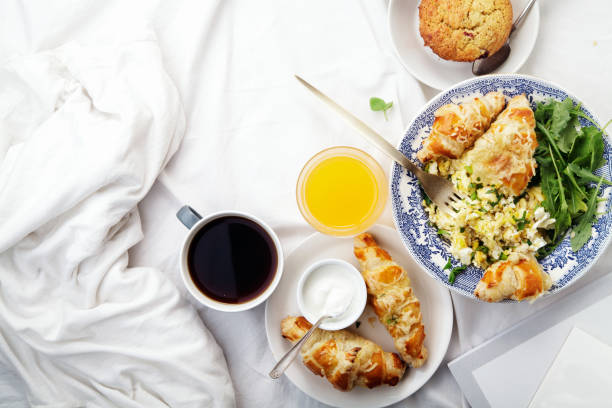 istock Breakfast in bed. Scrambled eggs with cheese croissants, raspberry muffin and black coffee. Lazy morning concept. Flat lay with copy space. 986540764
