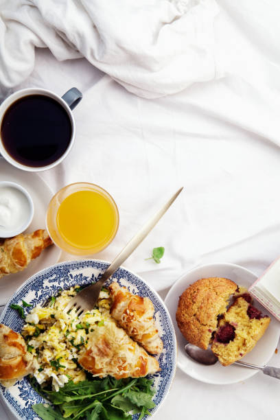 istock Breakfast in bed. Scrambled eggs with cheese croissants, raspberry muffin and black coffee. Morning treat concept. Composition with copy space. 986540776