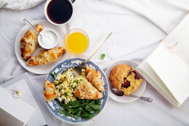 istock Breakfast in bed. Scrambled eggs with cheese croissants, raspberry muffin and black coffee. Lazy morning concept. Flat lay with copy space. 986540800