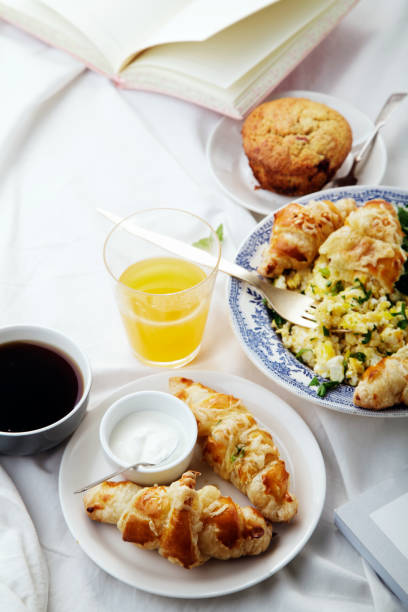 istock Breakfast in bed. Scrambled eggs with cheese croissants, raspberry muffin and black coffee. Morning treat concept. Side view with copy space. 986540834