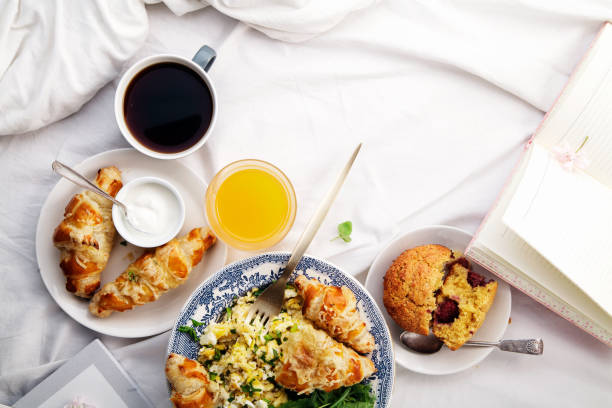 istock Breakfast in bed. Scrambled eggs with cheese croissants, raspberry muffin and black coffee. Morning treat concept. Composition with copy space. 986540840
