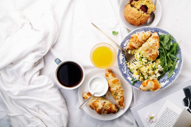 istock Breakfast in bed. Scrambled eggs with cheese croissants, raspberry muffin and black coffee. Morning treat concept. Composition with copy space. 986540888