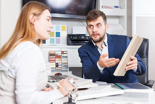 Young woman with salesman choosing material for new furniture in salon