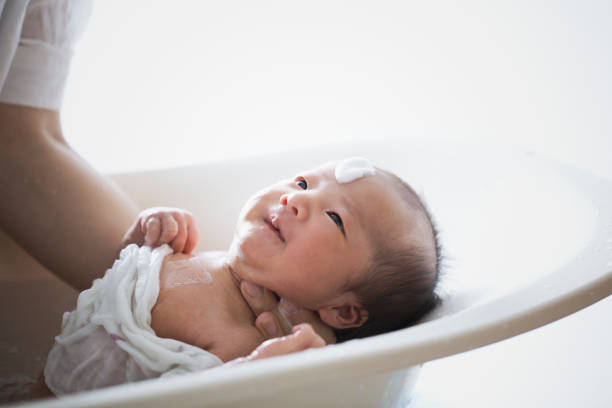 Mother bathing her baby girl at home An asian mother bathing her baby girl with baby bathtub. candid bonding connection togetherness stock pictures, royalty-free photos & images