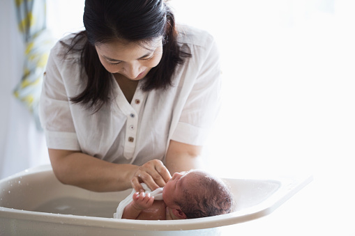 An asian mother bathing her baby girl with baby bathtub.