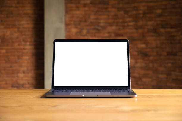 istock Mockup image of laptop with blank white desktop screen on wooden table with concrete wall background 986567186