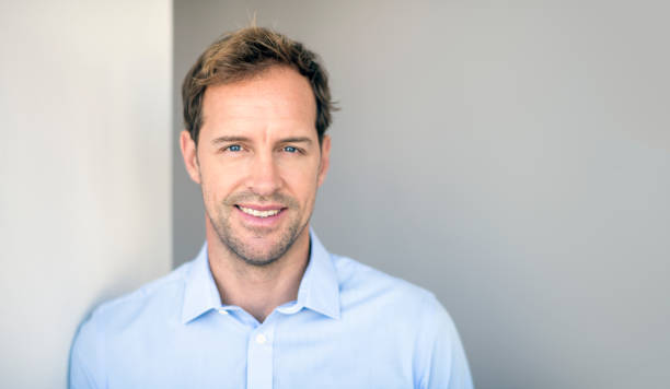 istock Smiling businessman standing against gray wall 986573822