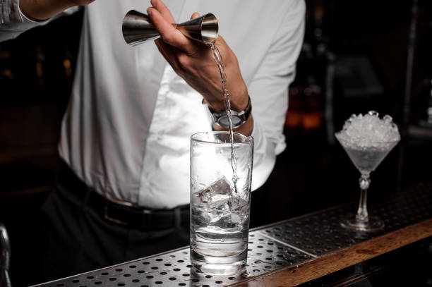 Bartender adding an alcoholic drink into the cocktail glass with ice