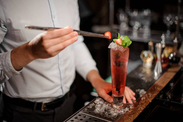 istock Barman adding a strawberry to the fresh transparent red cocktail 986594322