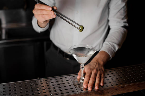 barista che aggiunge un'oliva nel bicchiere martini con una pinzetta - still shot foto e immagini stock