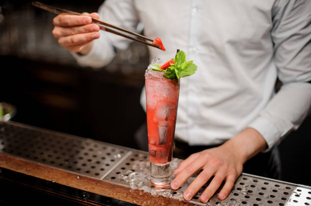 istock Barman adding a strawberry to the fresh transparent red cocktail with mint leaves 986601032