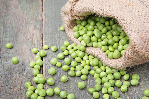 istock Fresh green peas in sackcloth on wooden table 986614256