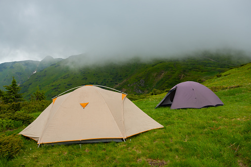 Tents on the green mountain meadow on the background green ridges in the fog - in the mountains before storm.