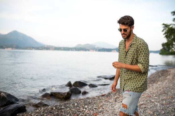 Handsome smiling man wearing sunglasses and looking away. He is sitting by the sea