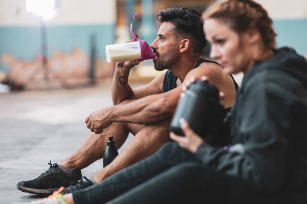Man and woman in sports clothing drinking protein drinks A man and a woman in sports clothing making and drinking protein drinks while sitting on the concrete floor. protein drink stock pictures, royalty-free photos & images