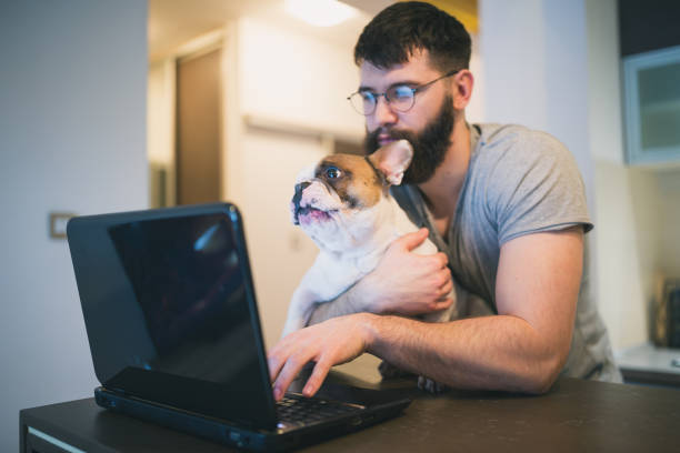 istock Handsome man browsing internet on laptop on kitchen counter with his dog 986649628