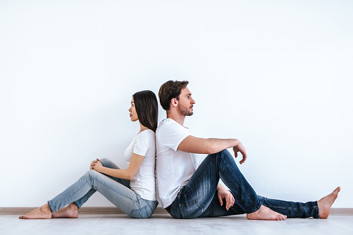 The attractive couple sitting on the floor on the white wall background