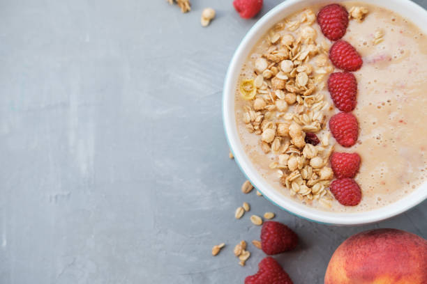 istock Peach smoothie bowl with granola and raspberry in a blue bowl on grey background. Top view. Healthy and colorful breakfast 986660230