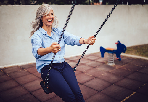 Active mature woman with gray hair relaxing and having fun at playground sitting on swing