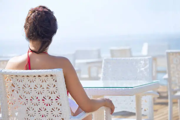 A woman sits alone in a restaurant on the beach and looks at the sea. The concept of enjoying solitude and tranquility.