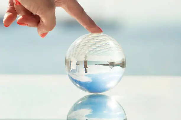 Concept of summer holidays and vacation trips. A female hand holds a glass bowl with reflection of the sea, yachts and sky.
Can illustrate the opening of the beach season.