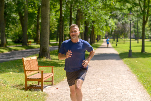 Middle aged man jogging along alley in park on sunny day in a close up view