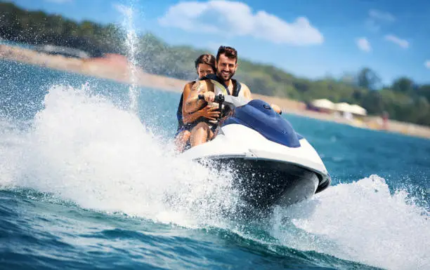 Closeup front view of a young couple riding a jet ski on a sunny summer day at open sea. The guy is driving and the girls is sitting behind.