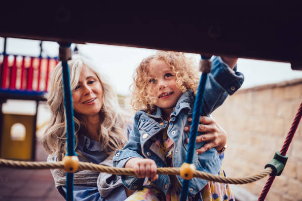 grandmother helping granddaughter climb rope ladder at playground jungle gym - child jungle gym playground laughing imagens e fotografias de stock