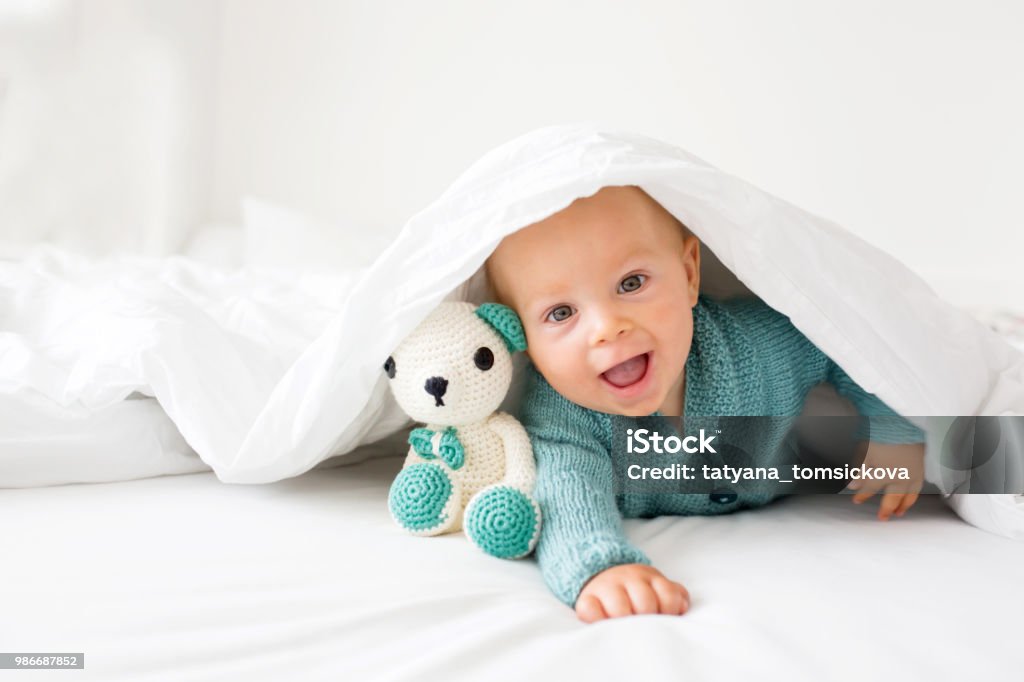 Little cute baby boy, child in knitted sweater, holding knitted toy, smiling happily at camera Little cute baby boy, child in knitted sweater, holding knitted toy, smiling happily at camera in white sunny, bright bedroom Baby - Human Age Stock Photo