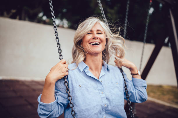 portrait of mature woman with gray hair sitting on swing - women mature adult happiness beautiful imagens e fotografias de stock