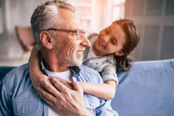 la ragazza felice abbraccia un nonno sul divano - grandpa portrait foto e immagini stock